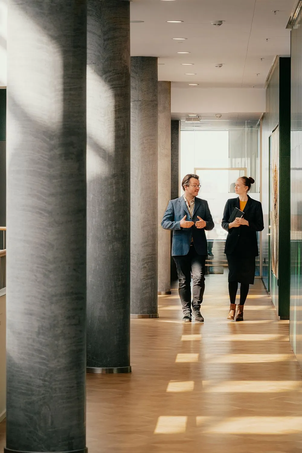 Twee collega's lopen pratend door een lichte kantoorgang